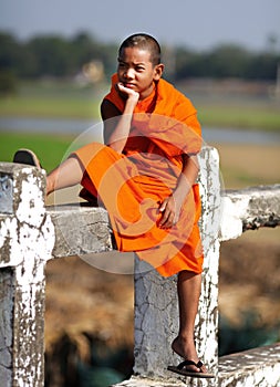 Young Buddhist monk sitting on a bridge