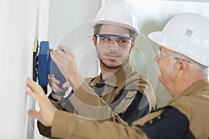 Young builder apprentice in hardhat sanding wall indoors