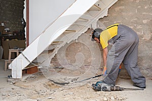 Young builder breaking up a house floor with a crowbar.