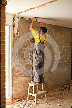 Young builder breaking up a house wall with a hammer and a chisel.