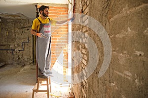 Young builder breaking up a house wall with a hammer and a chisel.