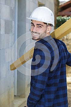 young builder carrying wood on shoulder