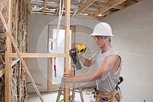 Young builder industry trainee man on his 20s wearing protective helmet learning working with drill at industrial workshop site