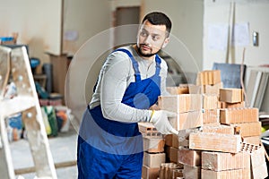 Young builder is laying bricks on top of each other