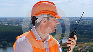 Young builder man wearing safety helmet and using walkie-talkie, discussing, standing outdoors. Business, building