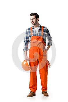 Young builder in orange overall holding hard hat