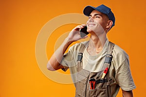 Young builder talking on a mobile phone against yellow background