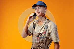 Young builder talking on a mobile phone against yellow background