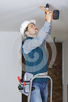 young builder up ladder drilling ceiling