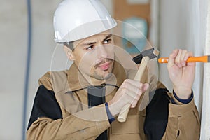 Young builder using hammer to remove plaster from wall