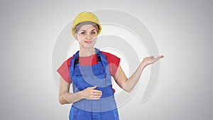 Young builder worker woman presenting showing product with her hands from her sides on gradient background.