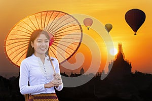 Young Burmese woman with a red umbrella. Young girl and Sunrise many hot air balloon with stupas in Bagan, Myanmar. space for text