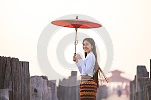 A young Burmese woman is walking with a red umbrella on the longest teak bridge in Asia.U-bein bridge, Mandalay, Myanmar