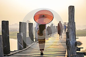 A young Burmese woman wearing traditional clothes with red umbrella at U Bein teak bridge in Mandalay Division. Myanmar photo