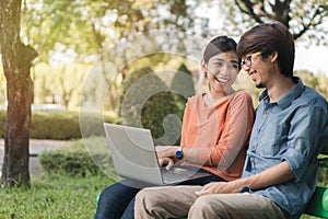 Young business asian man and woman working with them laptop and look at the face and smile together on a bench in the park