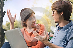 Young business asian man and woman working with them laptop and talking serious  on a bench in the park outdoors on vacation time