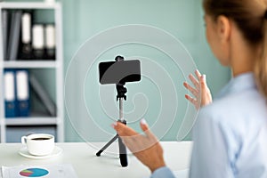 Young business blogger recording video on cellphone, talking to mobile phone with blank screen on tripod