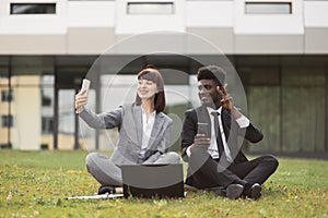 Young business colleagues having fun outdoors, sitting outside office and taking a selfie