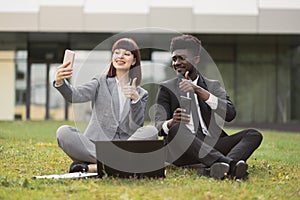 Young business colleagues having fun outdoors, sitting outside office and taking a selfie