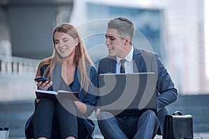 Young business couple reading online news near office building