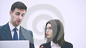 Young business couple standing, looking at something in the laptop, discussing important questions, thinking.