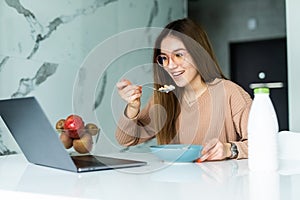 Young business entrepreneur woman working at home while having breakfast using laptop computer in the kitchen. Working online