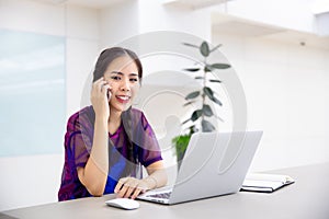 Young business female using smart phone while working on computer laptop