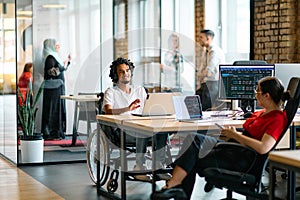 A young business group, including an African American businessman in a wheelchair, collaborates within a modern glass