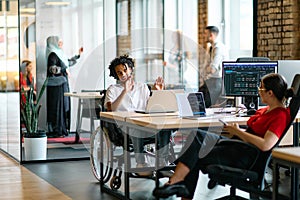 A young business group, including an African American businessman in a wheelchair, collaborates within a modern glass