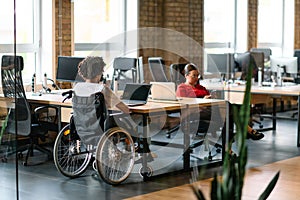 A young business group, including an African American businessman in a wheelchair, collaborates within a modern glass