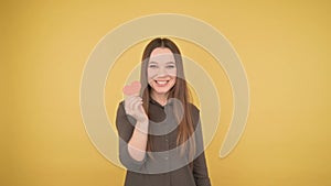 Young business lady covered mouth small paper red heart on yellow background