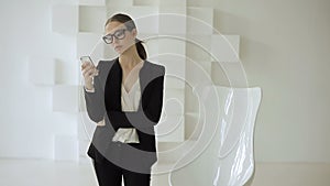 Young business lady stands with a mobile near a white chair in a futuristic white office