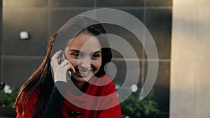 Young business lady talking on a cell phone sitting at a table in a cafe on the street.