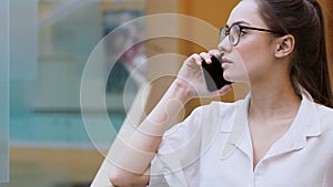 Young business lady uses a smartphone. A girl in a white shirt and glasses makes a phone call.