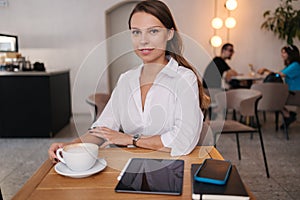 Young business lady working in cafe. Attractive woman in white shirt. Formal portrait