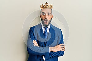 Young business man with beard wearing king crown afraid and shocked with surprise and amazed expression, fear and excited face