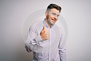 Young business man with blue eyes standing over isolated background doing happy thumbs up gesture with hand