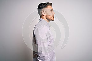 Young business man with blue eyes standing over isolated background looking to side, relax profile pose with natural face with