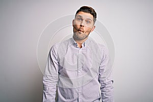 Young business man with blue eyes standing over isolated background making fish face with lips, crazy and comical gesture