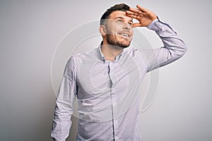 Young business man with blue eyes standing over isolated background very happy and smiling looking far away with hand over head