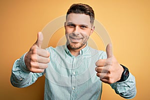 Young business man with blue eyes wearing elegant green shirt over yellow background approving doing positive gesture with hand,