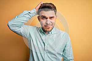 Young business man with blue eyes wearing elegant green shirt over yellow background confuse and wonder about question