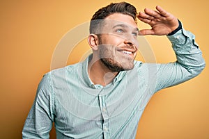 Young business man with blue eyes wearing elegant green shirt over yellow background very happy and smiling looking far away with