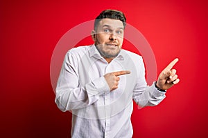 Young business man with blue eyes wearing elegant shirt standing over red isolated background Pointing aside worried and nervous