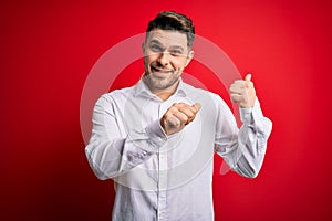 Young business man with blue eyes wearing elegant shirt standing over red isolated background Pointing to the back behind with