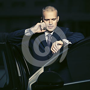 Young business man calling on cell phone outside a his car