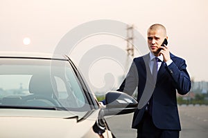 Young business man calling on the phone next to car
