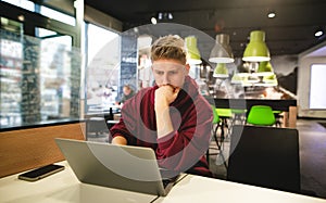 Young business man in casual clothing works in a cafe on a laptop, focuses on looking at the screen. Freelancer works in a fast