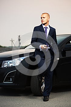 Young businessman with a cell phone leaning on his car