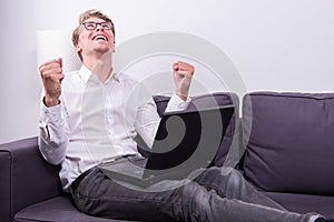 Young business man cheering his success while working on laptop
